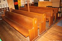 Row of wooden church pews with solid backs and seats, medium brown finish, showing their length and size on wooden floor.