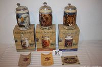 Front view of three Budweiser ceramic steins featuring Bald Eagle, Grizzly Bear, and Cougar designs with original boxes below and three tags/certifications in front.