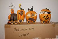 The fully assembled Halloween pumpkin train displayed on a box labeled 'Halloween Train'. Train has four distinct cars with various pumpkin and Halloween themed decorations including bats, ghosts, a black cat, and jack-o'-lantern faces.