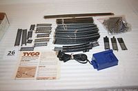Top-down photo showing all the track pieces, the blue Life-Like power pack with attached cord, bag of trestle pieces, and TYCO instruction sheets.