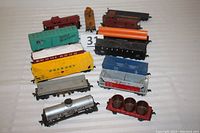 Top view of 12 HO scale train cars showing various types including coal cars, tankers, flatcars, cabooses, and search light car with visible couplers and wheel sets.