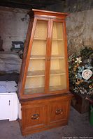 Front view of the mid-century modern solid wood curio cabinet with mesh door panels, showing its tapered shape and base with two cabinet doors.