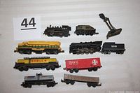 Photo showing three N-scale model train engines (1 diesel, 2 steam with tenders) and four rolling stock cars from different railroads including Shell, Santa Fe, and Southern.