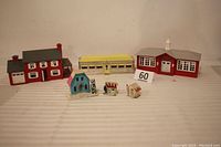 Group photo showing all six structures together: three Plasticville O Scale structures including a diner, house, and school building along with three smaller Putz houses in front.