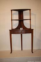 Front view of assembled table with shelf unit on top, showing two shelves and one drawer below.