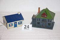 View of two metal/tin Lionel buildings: larger No. 191 Villa with green roof and smaller blue and white building with dark blue roof, displayed side by side on white background.