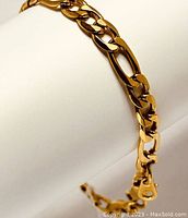 Close-up of the gold plated Figaro chain bracelet detail on a white display.