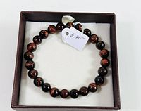 Top view of the red tiger eye beaded bracelet presented in a brown jewelry box with white padding, showing the uniform round beads and price tag of $18.00.