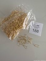 Large plastic bag full of gold-tone metal gourd shaped safety pins with some pins out of the bag shown.