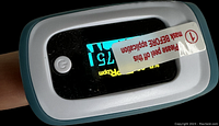 Close-up photo showing pulse oximeter device powered on and measuring pulse rate and oxygen saturation.