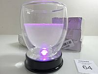 Clear double-wall glass cup on LED light display stand base showing purple LED light illumination. Box and battery compartment visible in background.