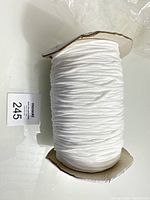 Side view of white elastic cord wound on spool with visible folds and texture showing 3mm thickness.