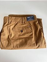 Folded tan men's pants showing the back view with a buttoned back pocket and Tommy Hilfiger logo.