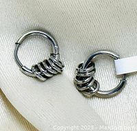 Close-up front photo showing pair of silver hoop earrings with coil design placed on beige surface