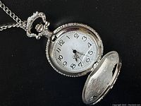 Close-up of the open pocket watch face showing white dial, black numbers and decorative hands.