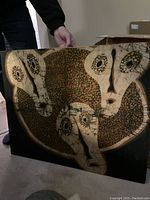 African batik fabric print with abstract faces in earth tones on wood frame held partially up