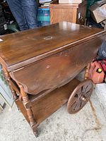 Photo of wood accent table showing drop-leaf sides with curved edges, large wooden wheels, and visible surface damage on top.
