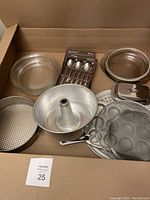 Overview of bakeware and kitchen tools including pie plates, cake pans, butter dish, spoons, and cheese cutting tools arranged in a box