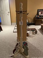 Full view of the cream-colored wooden children's coat stand with four metal hooks at the top and animal figures at the base.
