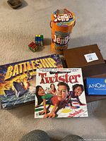 Overview photo showing Battleship, Twister, Anomia, two Jenga sets, two Rubik's Cubes, and a closed brown leather backgammon case.