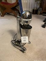 Full view of the Hamilton Beach Classic 2-speed shake blender placed on carpet next to power cord and stainless steel cup attached.