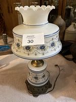 Full view of the glass and brass lamp showing the ruffled white glass top, floral decorated glass shade and base with brass stand and base.