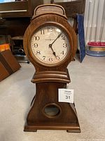 Full frontal view of the wooden mantel clock showing the clock face, base, and pendulum window.