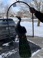 Full view of the colorful papier-mâché peacock mounted on black metal hanging frame.