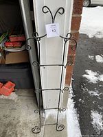 Photo of black metal wall-mounted plate rack designed to hold 4 decorative plates, showing hooks and rails in an outdoor setting.