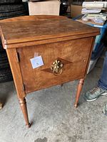 Closed view of the wooden cabinet housing the sewing machine, showing decorative brass handle on door and medium brown finish.