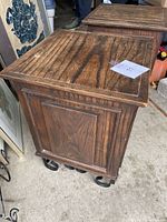Full view of one wooden side table showing paneled side and wood grain top with some wear.