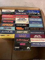 Full view of 32 VHS movies in box showing titles on VHS spines