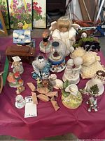 Full view of animal and people figurines, wind-up musical dolls, wooden puzzle, Swarovski owl, tealight holder, and miscellaneous figurines on pink cloth surface.