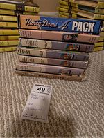 Stack of books showing Nancy Drew 4-pack, Bobsey Twins books with visible water damage and wear, Nancy Drew Cookbook, and a CD case.