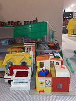 Side view showing a yellow roof Play Family House, red and white fire truck, and part of a multilevel building with figures on top