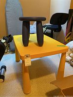Yellow child's plastic table with thick legs and small dark gray stool on top, showing marks and scratches.