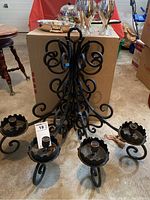 Front and side views of the metal candleholder showing the four candle cups and scrollwork design with some rust and dust.