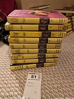 Stack of Nancy Drew books with yellow spines, showing age wear. Books arranged horizontally on carpeted floor.