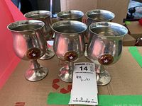Six pewter chalices arranged in two rows on a cardboard surface. Each chalice has a rounded shape with a star medallion on the front. The image highlights the overall look and condition of the lot showing some fading and wear.