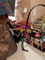 Photo showing a collection of womens purses and wallets on the floor including a large brown embossed purse, colorful handbag, and smaller wallets in mixed colors.