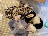Stuffed animals including a spotted leopard, black and white plush animal, and gray elephant on carpet