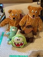 Overview of all five stuffed items including two large brown bears, a small turquoise bear, a small green round monster plush, and a small brown hooded figure.