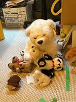 Photo showing the lot of stuffed animals arranged on carpet, including large white bear holding smaller beige bear, and other smaller plush bears and animals.