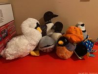 Group of stuffed animals including white swan, various birds, gray whale, and fish plush in a pile