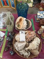 Overview of lot showing basket with seashells, blue art glass vase, white purse-shaped art glass vase, napkin rings, and small marble-like items.