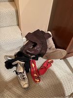 Six pairs of women's shoes and boots in various styles and colors including beige Ugg boots, brown boots, silver shoes with pom-poms, and red embroidered flats arranged on carpet.