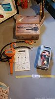 Full lot showing the 3/4 ton orange ratchet lever hoist with chain, original box, instruction manual, and the 4 ton hydraulic bottle jack in its plastic case.