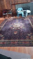 Rug laid on hardwood floor with chairs and fireplace in background, showing full layout and medallion center
