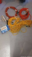 Image showing orange and yellow extension cords coiled and tied, a trouble light, and blue box on concrete floor.