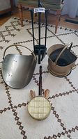 Photo showing the full set of fireplace accessories including brass coal shuttle, brass log carrier, fireplace tool stand with tools, brass match holder on the carpet.